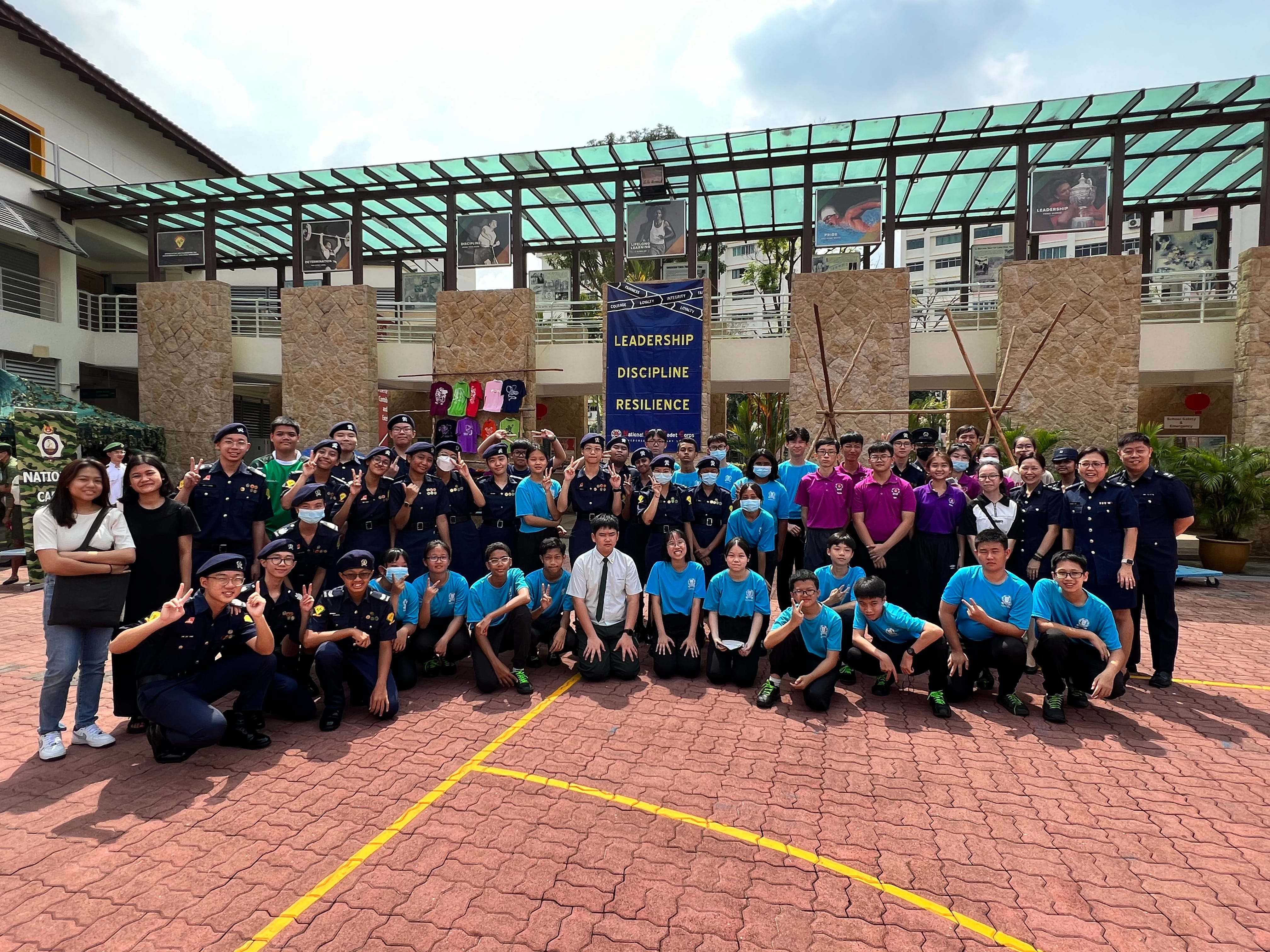 Large group of youth in uniforms posing outdoors near a banner reading Leadership, Discipline, Resilience.